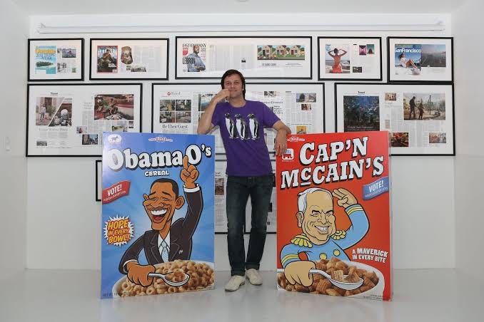 An Airbnb founder standing between giant Obama O's and Cap'n McCain's cereal boxes.